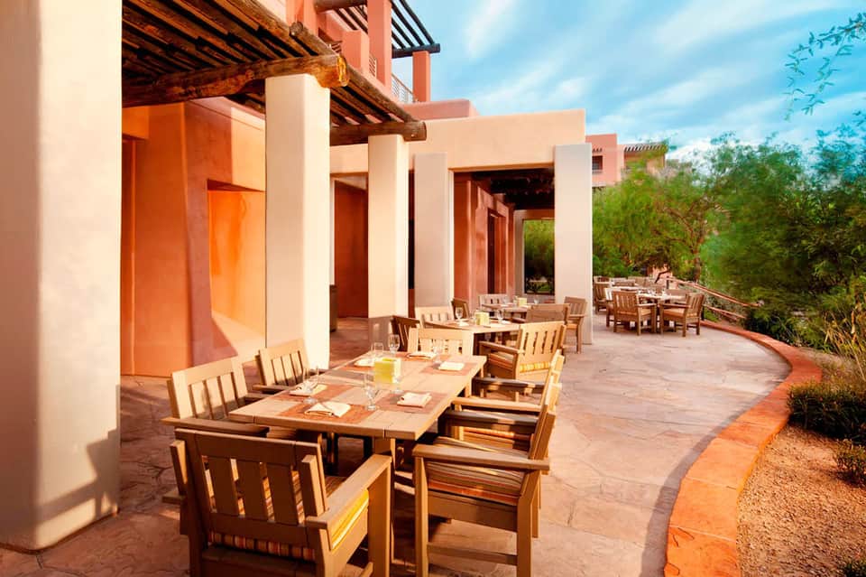 Outdoor terrace dining area with wooden tables, chairs, and desert resort architecture