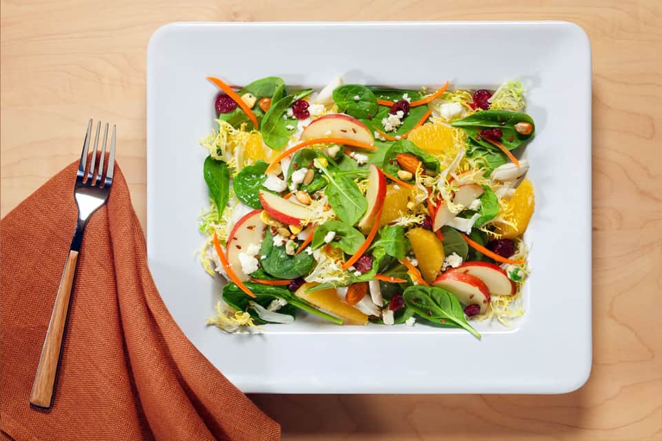 Colorful fresh salad with mixed greens, citrus slices, vegetables, and crumbled cheese on white plate