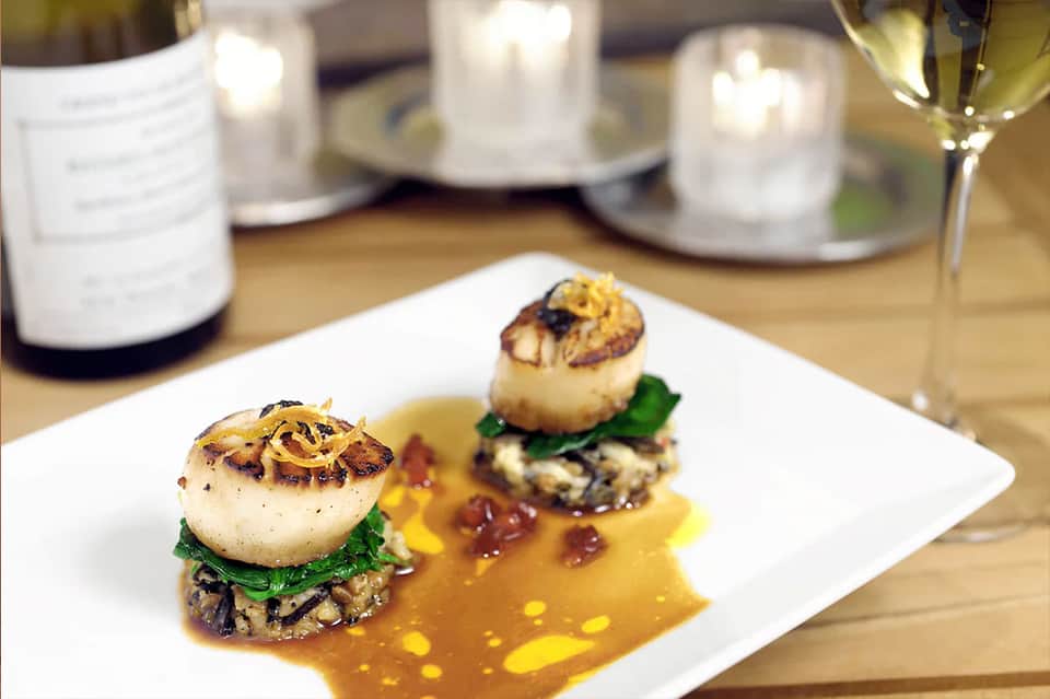 Plated fine dining dish with scallops, greens, and sauce with wine pairing