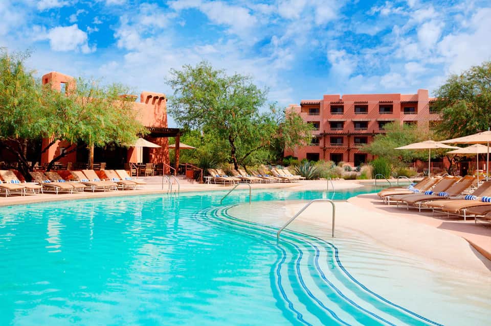 Resort pool with turquoise water, terracotta buildings, lounge chairs, and desert landscaping