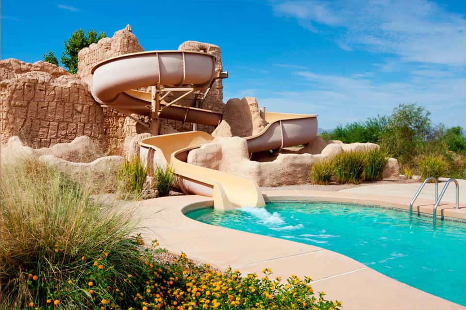 Water slide into turquoise pool at resort with desert rock formations