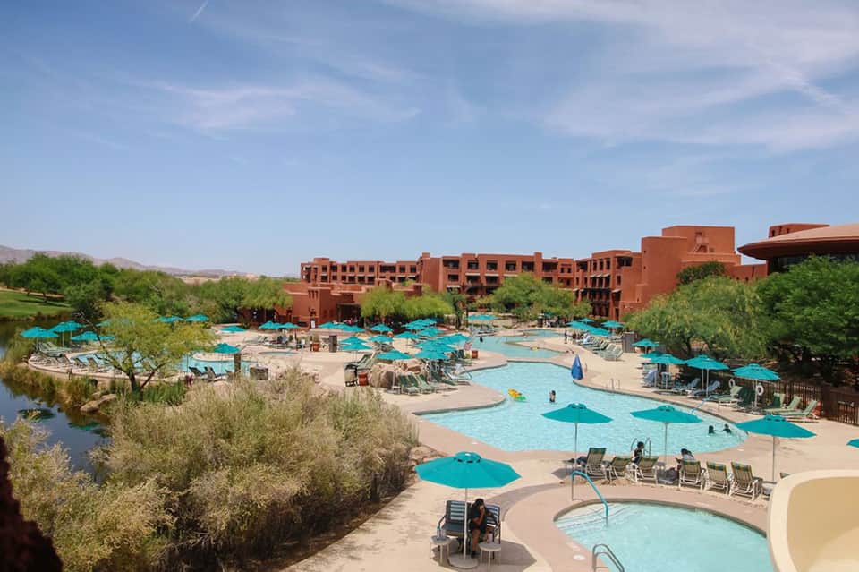 Large resort pool complex with turquoise umbrellas, red architecture, and desert landscape