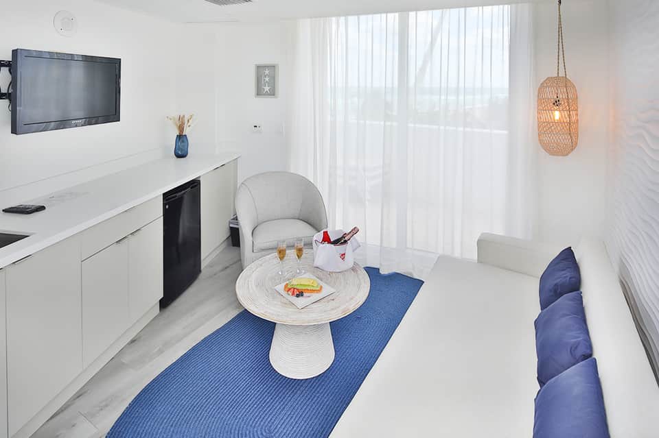 Modern resort suite with kitchenette, white furnishings, and ocean view