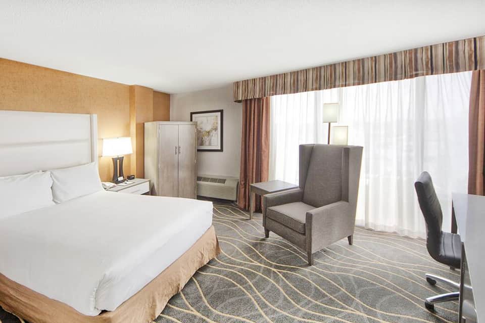 Hotel room with white bedding, gold accent wall, sitting area with windows, and modern décor