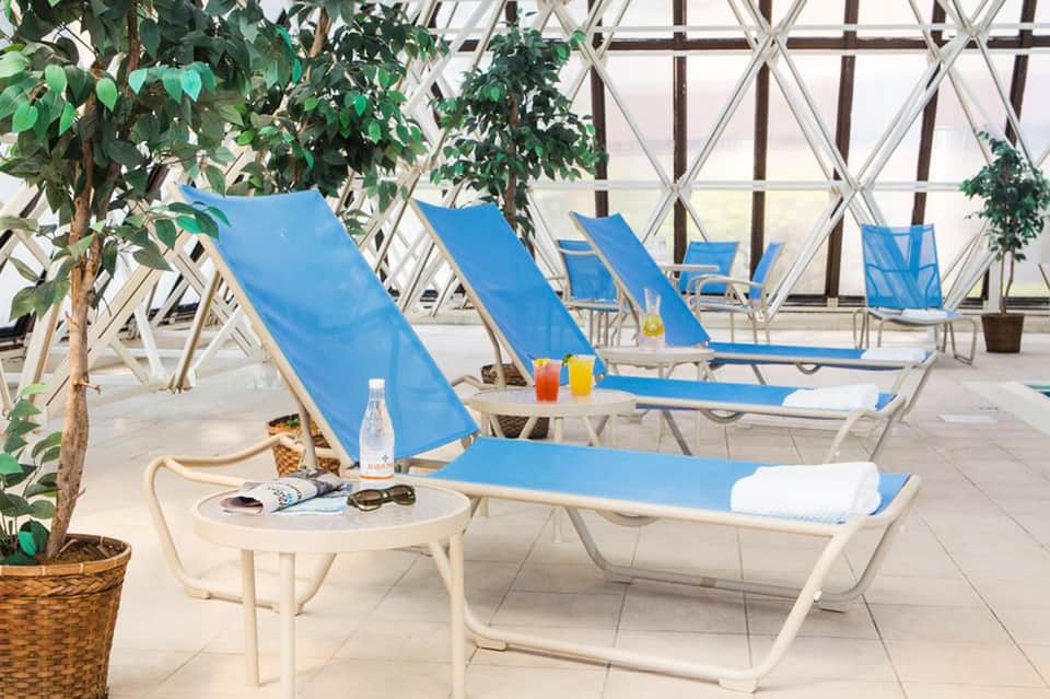Indoor spa lounge with blue recliners, white lattice windows, and potted plants