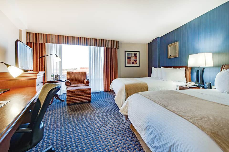 Hotel guest room with two queen beds, ocean view, and warm wood furnishings