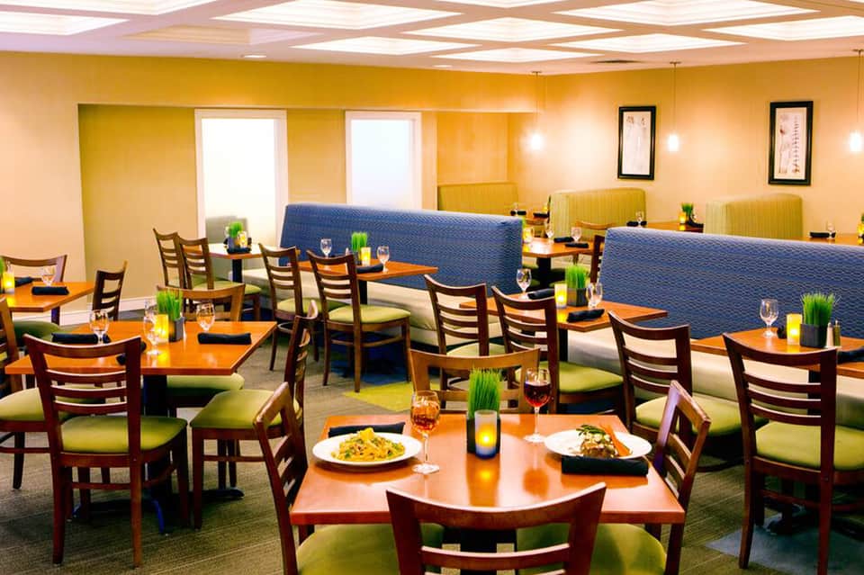 Bright dining room with orange tables, green cushioned chairs, and blue booth seating