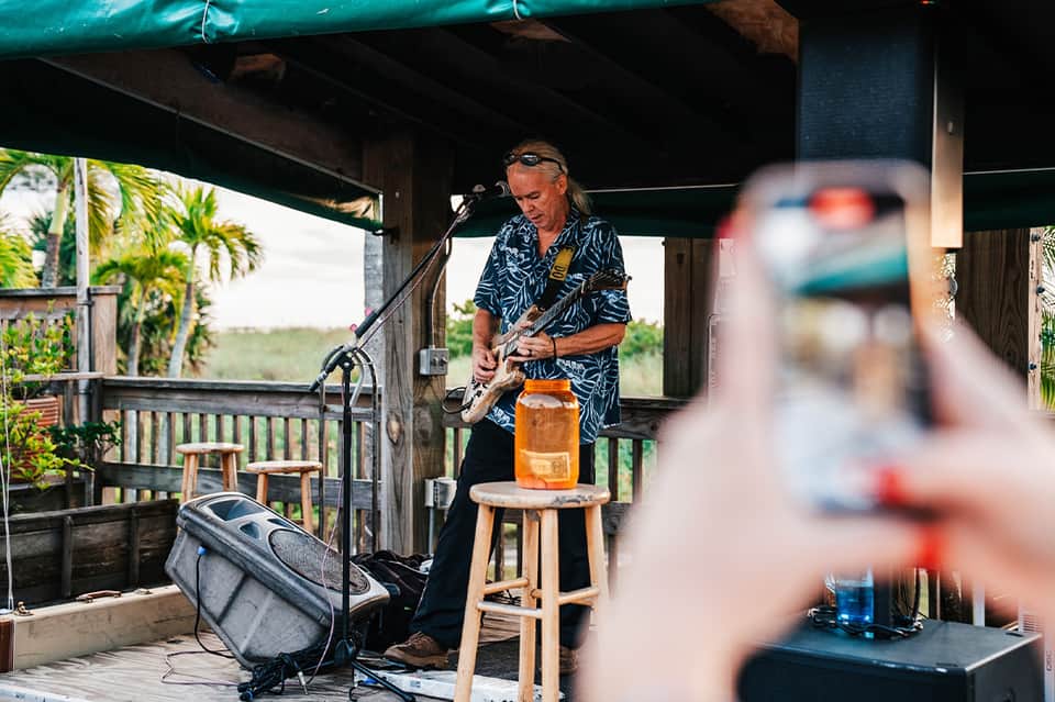 Live musician performing with guitar on covered pavilion overlooking tropical landscape