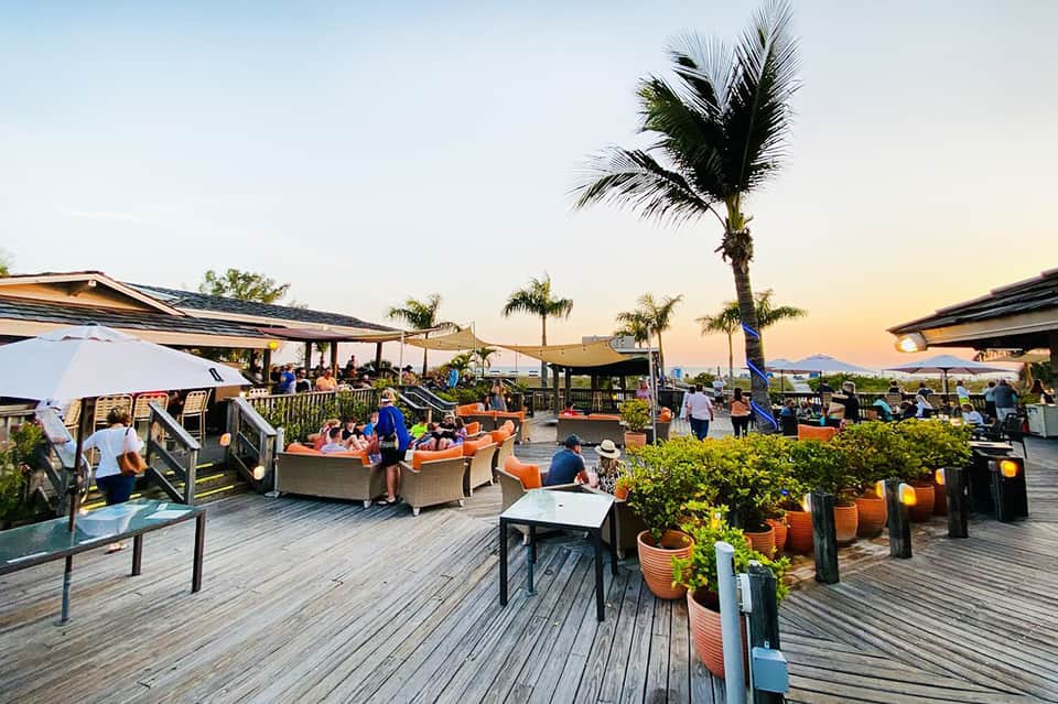 Sunset rooftop lounge with coral furniture, palm trees, and mountain views with guests relaxing