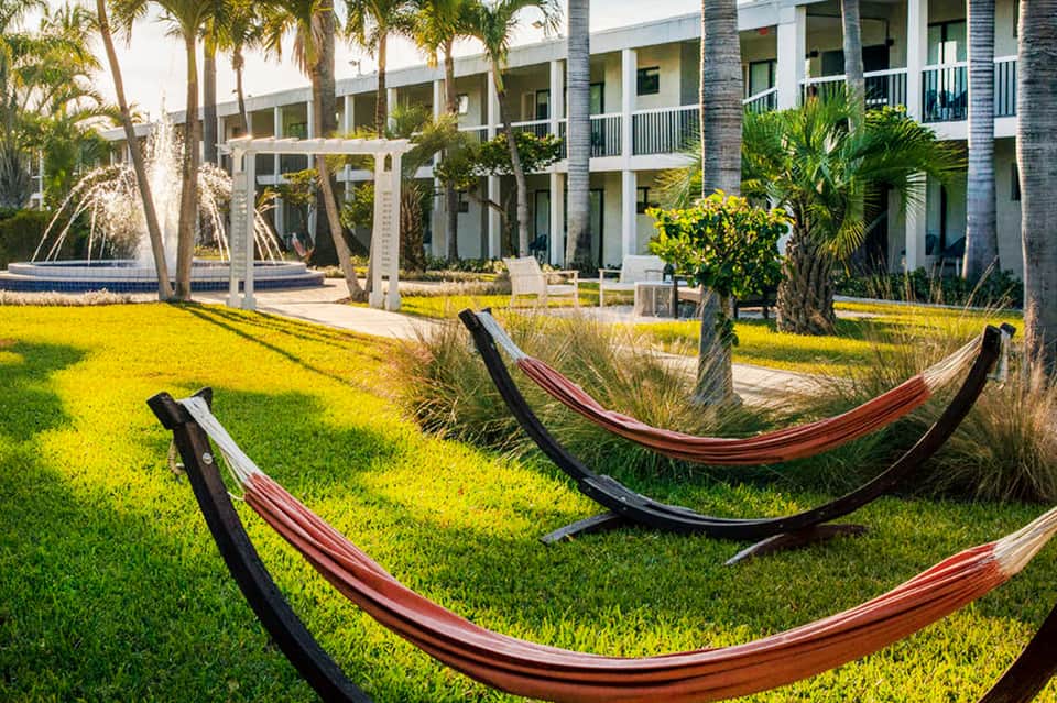 Resort grounds with red hammocks on manicured lawn, palm trees, and colonial-style buildings.