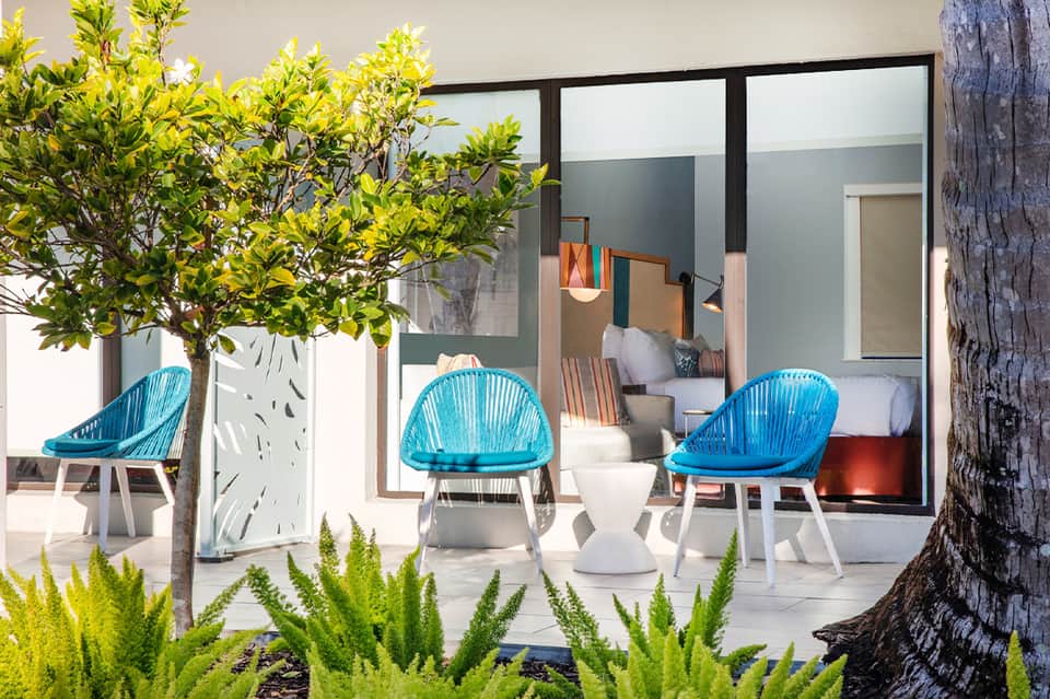 Modern outdoor patio with turquoise woven chairs, potted plants, and floor-to-ceiling glass doors