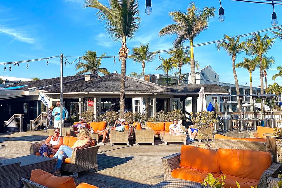 Beachfront boardwalk lounge area with orange seating, palm trees, and hanging lights