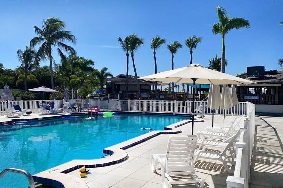 Resort pool with turquoise water, white umbrellas, palm trees, and beachfront pavilions