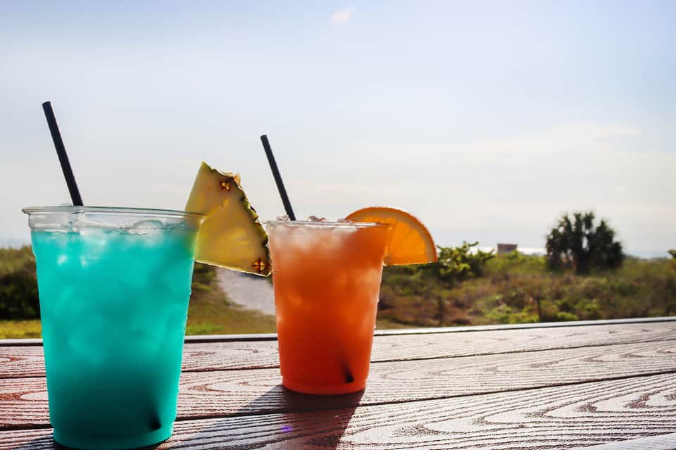Two tropical cocktails with colorful straws and fruit garnishes on wooden deck