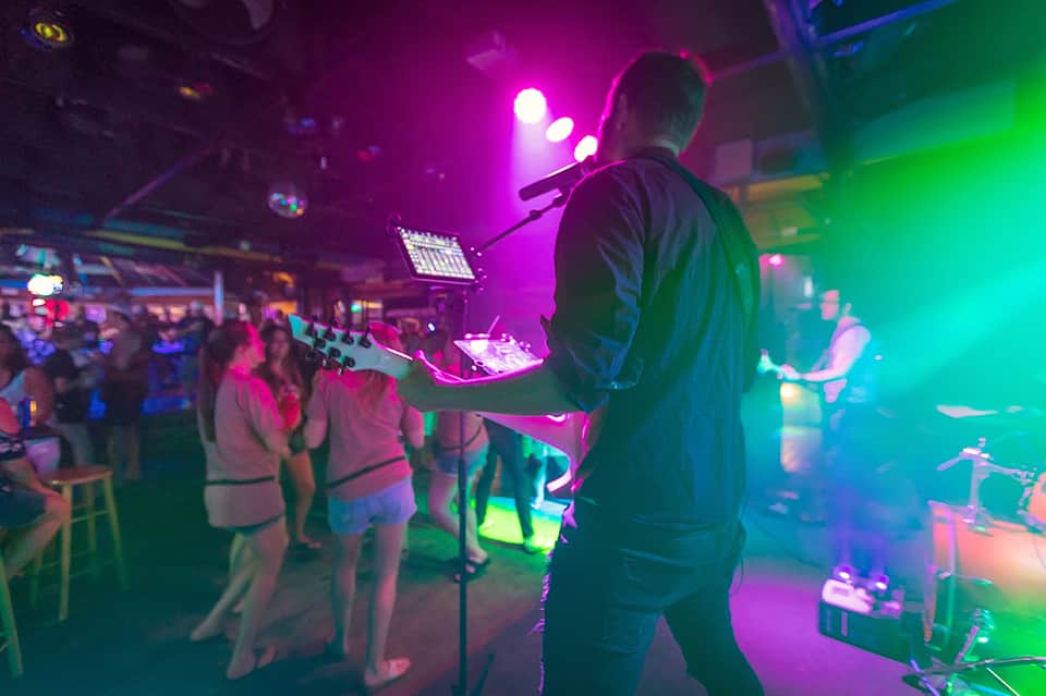 Nightclub dance floor with DJ on stage, colorful neon lighting in magenta and green, and dancing crowd