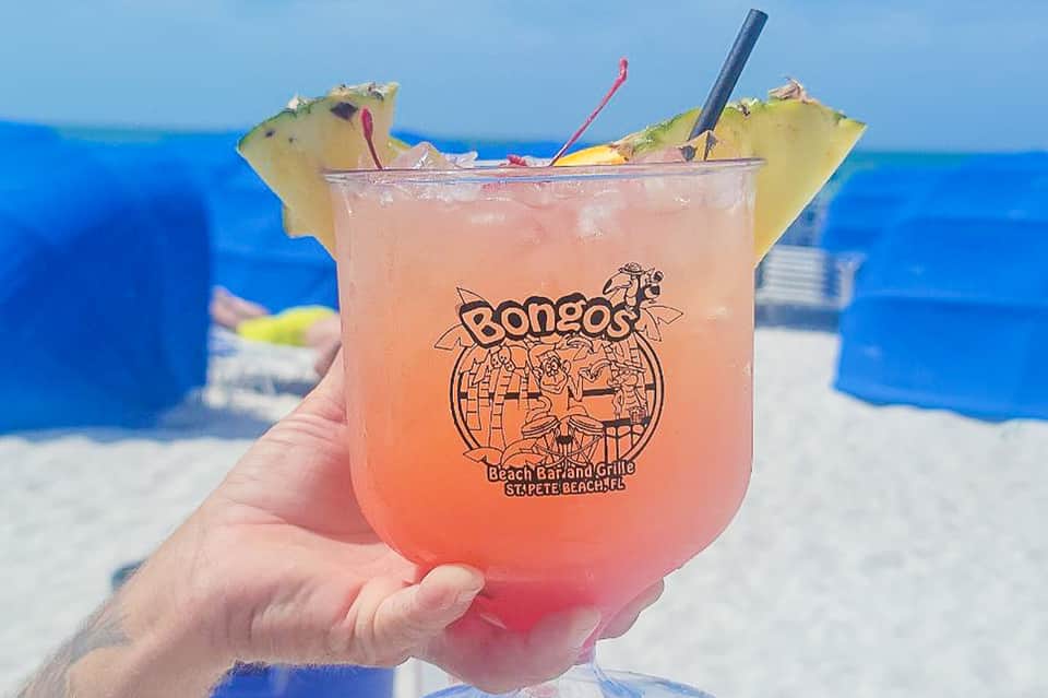 Pink tropical cocktail with pineapple garnish at beach bar with ocean and blue sky in background