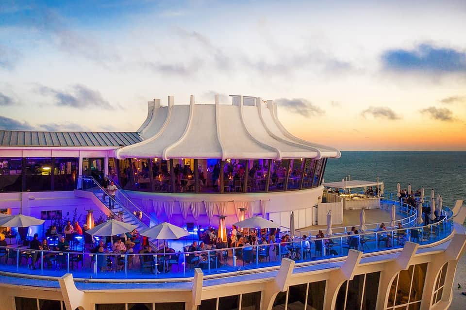 Modern rooftop bar and restaurant overlooking ocean at sunset with purple lighting