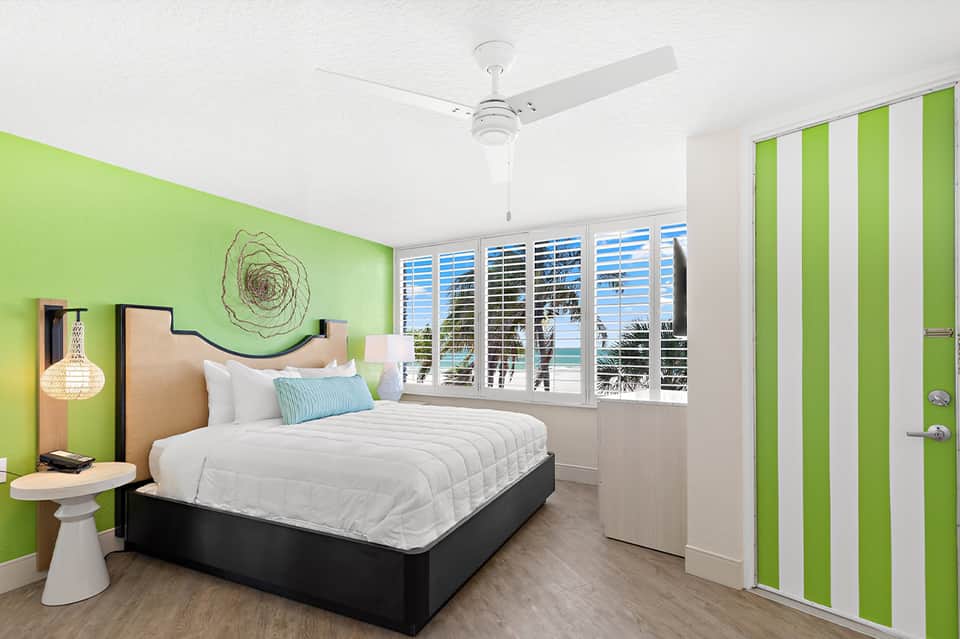 Modern hotel bedroom with lime green walls, white bedding, and ocean view