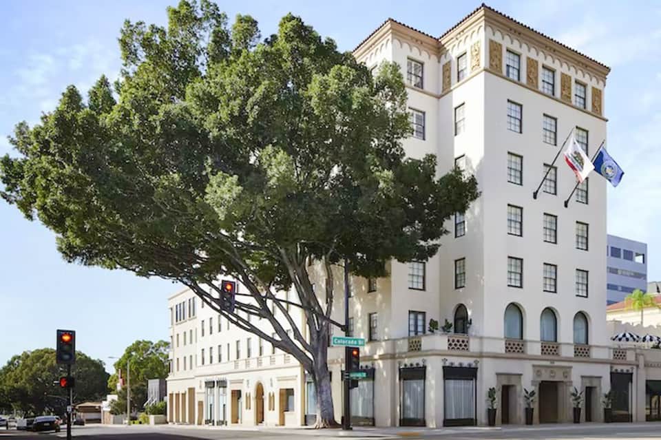 Historic white Spanish-style hotel building with ornate tower and large shade tree at street level