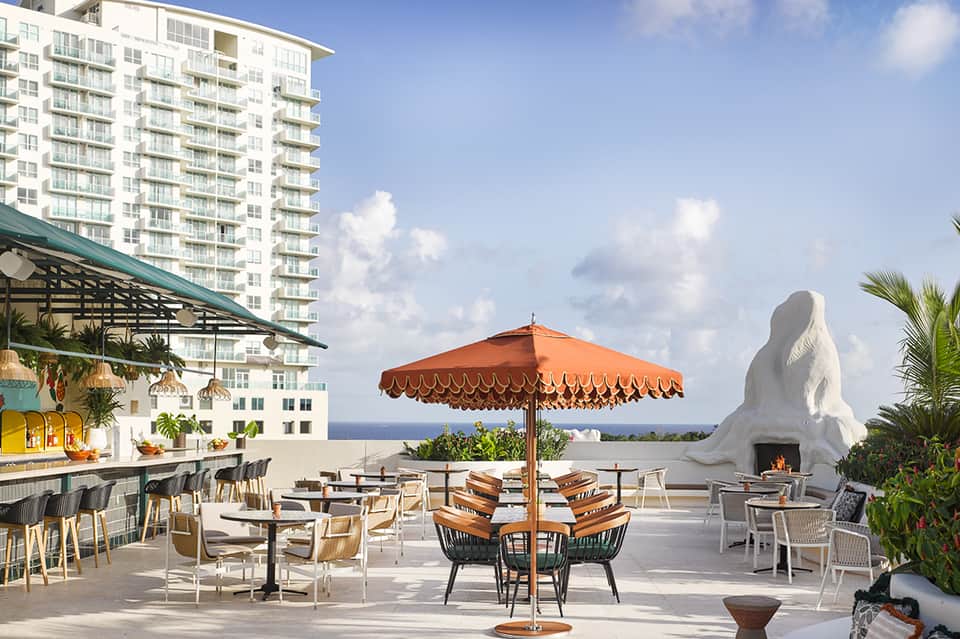 Beachfront resort terrace with orange umbrella, fire pit, and ocean view with modern architecture.