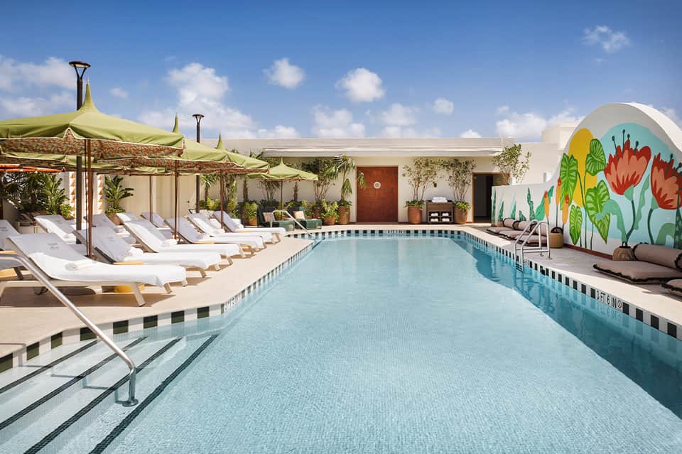 Resort pool with yellow umbrellas, lounge chairs, colorful mural wall, and clear sky