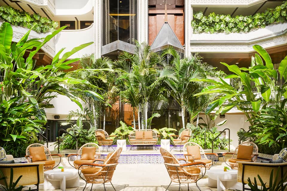 Elegant indoor courtyard with tropical plants, wrapped ceiling details, and rattan seating