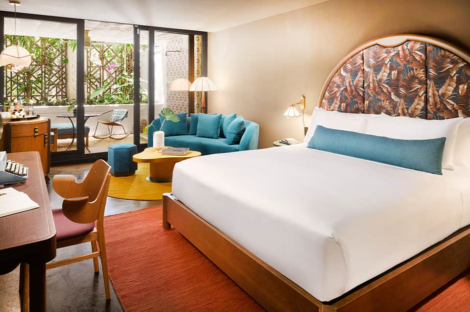 Luxury hotel bedroom with king bed, turquoise accents, patterned headboard, and ocean-view balcony