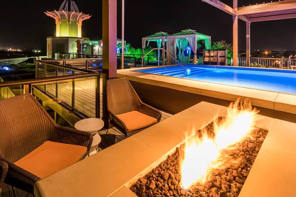 Illuminated pool deck at night with fire pit, lounge chairs, and decorative lighting