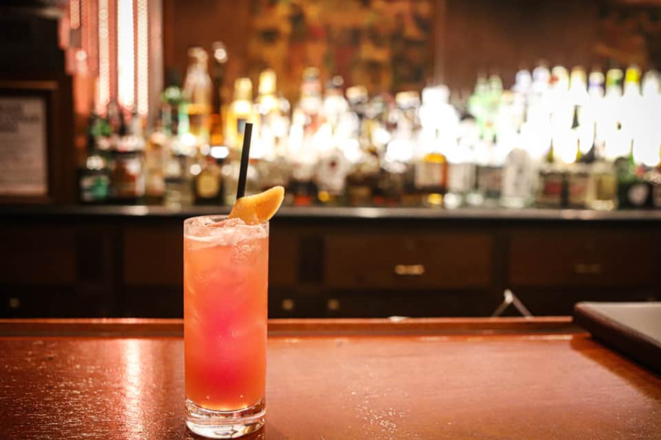 Tropical cocktail with orange garnish on bar counter with blurred bottles behind
