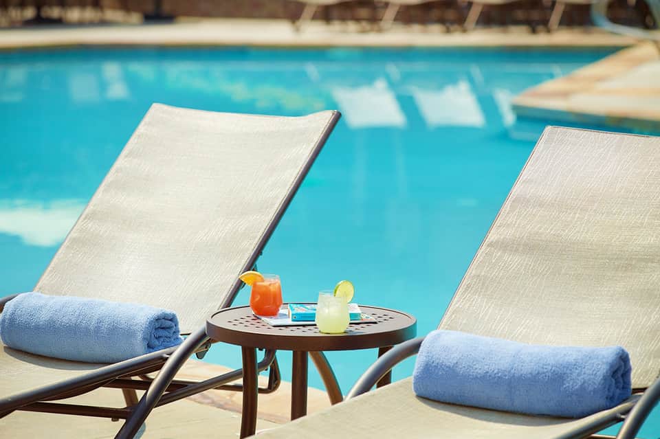 Poolside lounge chairs with blue towels and tropical cocktails overlooking bright turquoise pool