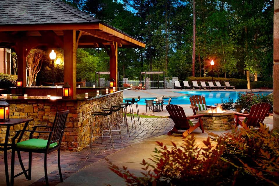 Illuminated poolside bar and lounge area at night with fire pit seating