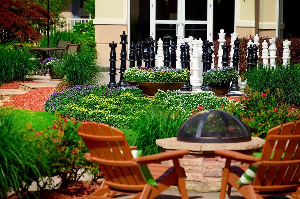 Garden courtyard with fire pit, colorful flowers, and large chess pieces