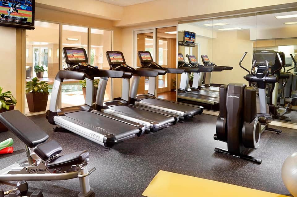 Bright fitness center with multiple treadmills, exercise bikes, and mirrored walls with glass partition