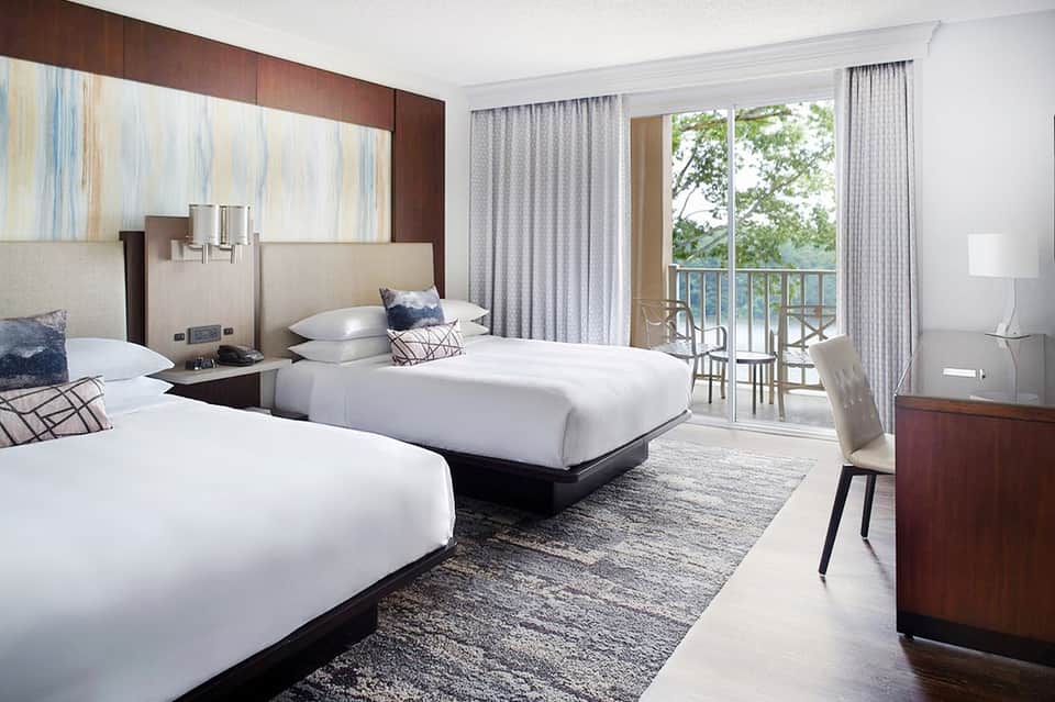 Contemporary hotel room with two beds, ocean-view balcony, and modern furnishings in neutral tones