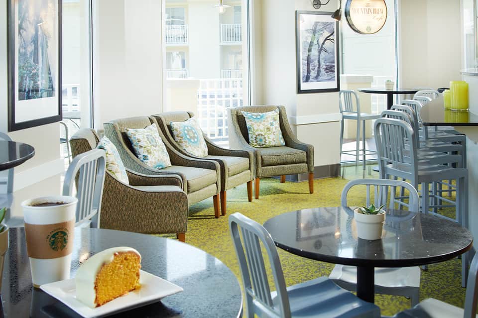 Bright café lounge with upholstered seating, large windows, and high-rise city views