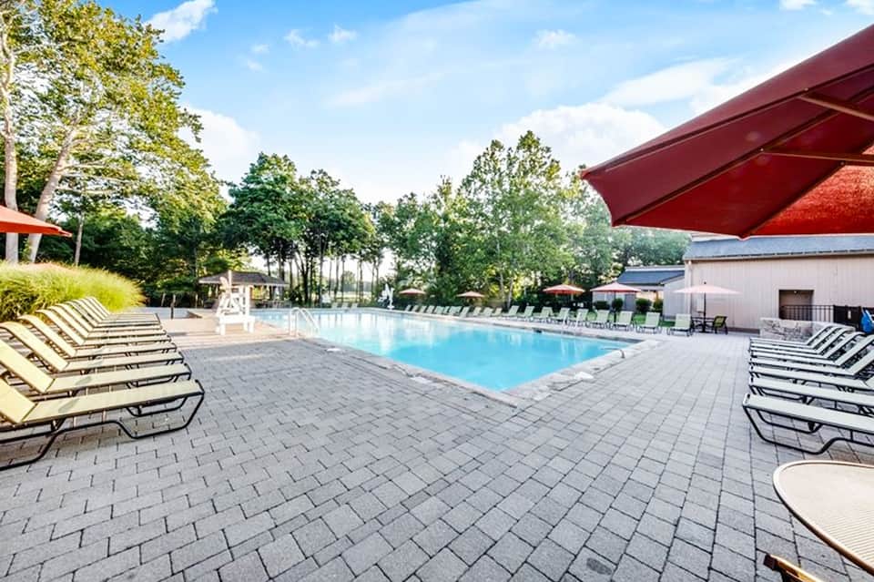Resort swimming pool with lounge chairs, paver deck, and wooded landscape under clear sky