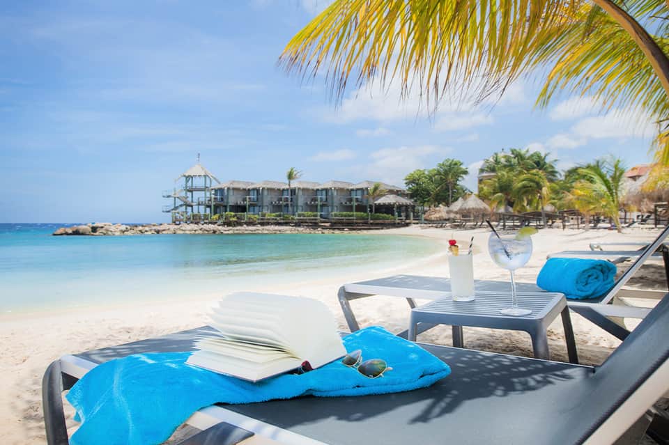 Beach lounge setting with cocktail, book, and towel overlooking tropical waters
