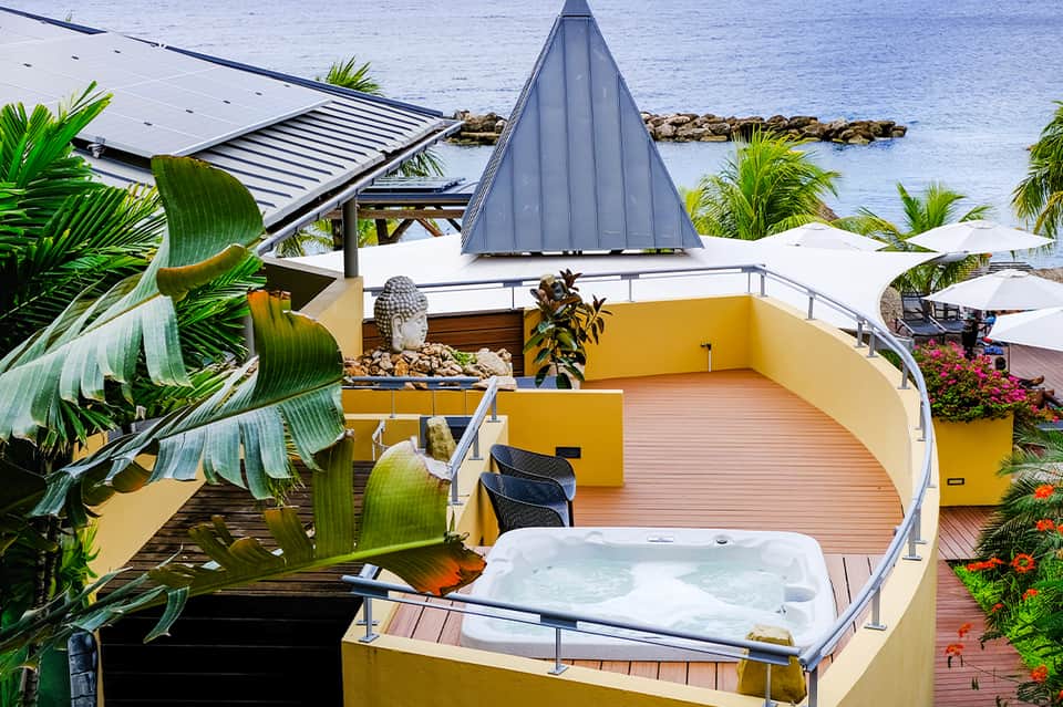 Oceanfront deck with hot tub, yellow walls, and palm trees overlooking blue water