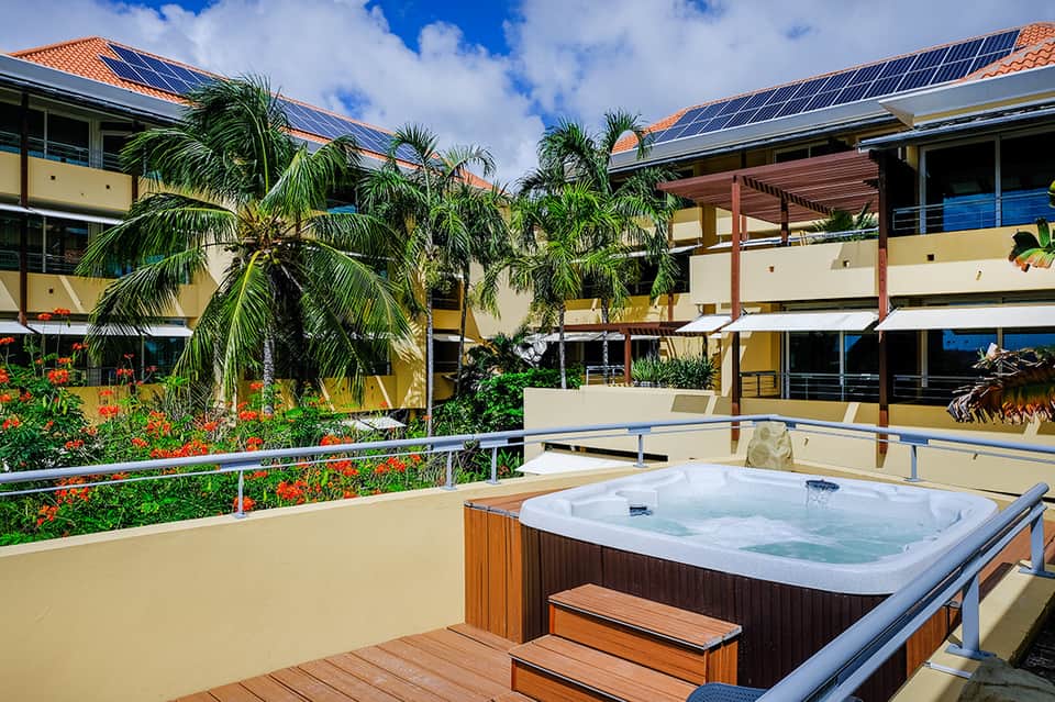 Rooftop hot tub with ocean view, palm trees, and modern resort building with solar panels