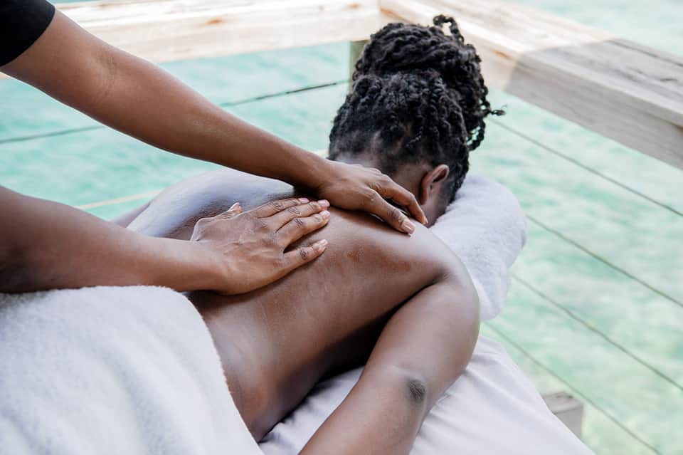 Spa therapist giving shoulder massage to woman poolside on white towel