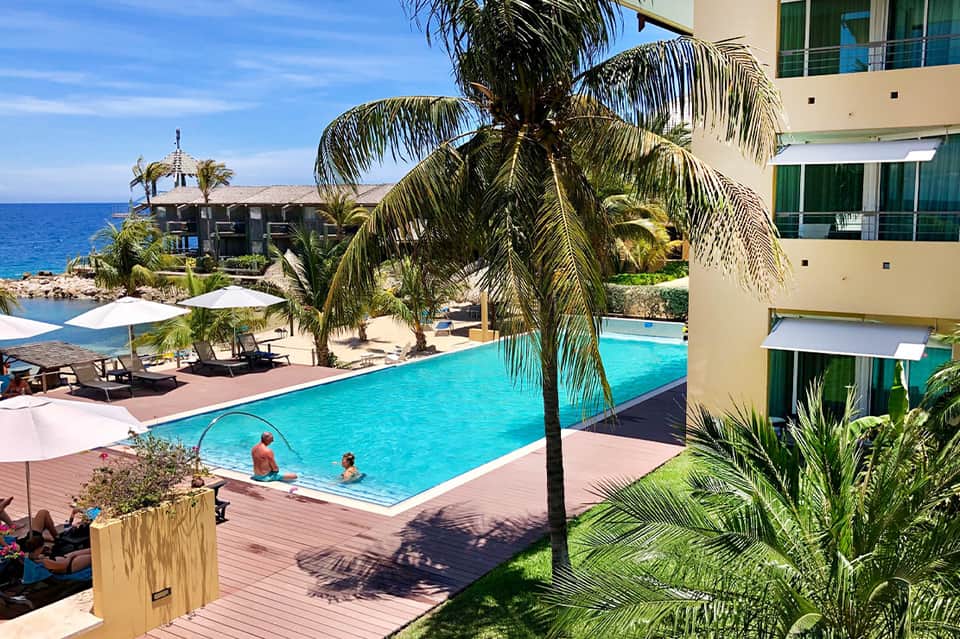 Resort pool with turquoise water, palm trees, and coastal ocean view