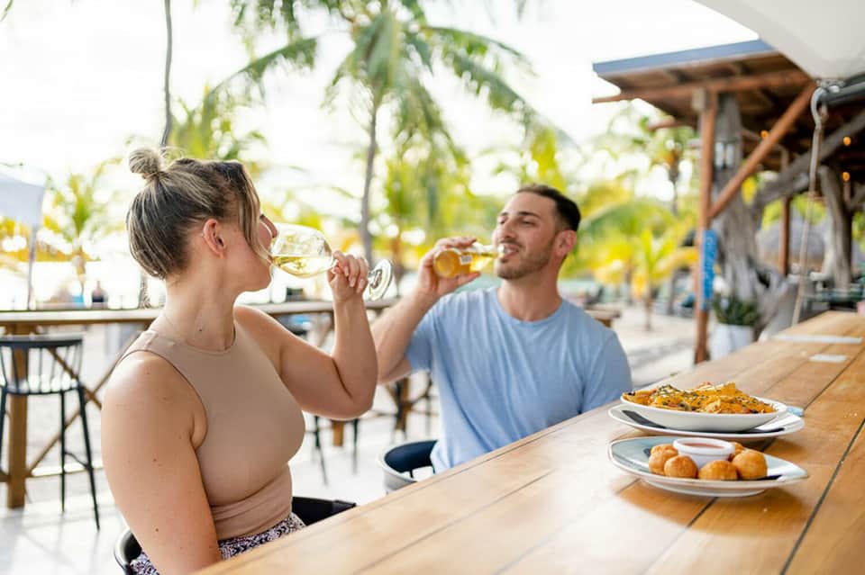 Couple dining and drinking wine at beachside restaurant with palm trees and ocean backdrop