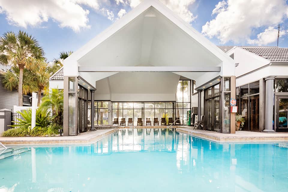 Indoor pool with glass ceiling, white architectural structure, and palm trees