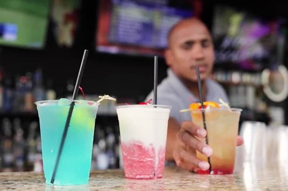 Bartender pouring colorful tropical cocktails with blue, pink, and amber colored drinks