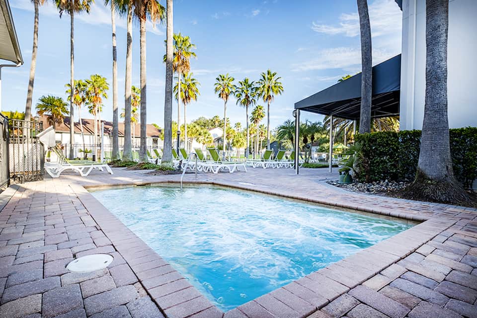 Resort pool surrounded by palm trees, lounge chairs, and covered cabana areas