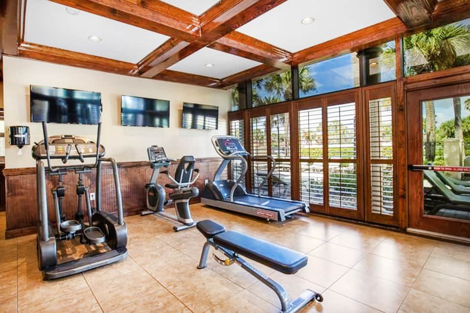Fitness center with wooden beams, exercise equipment, and large windows with outdoor views