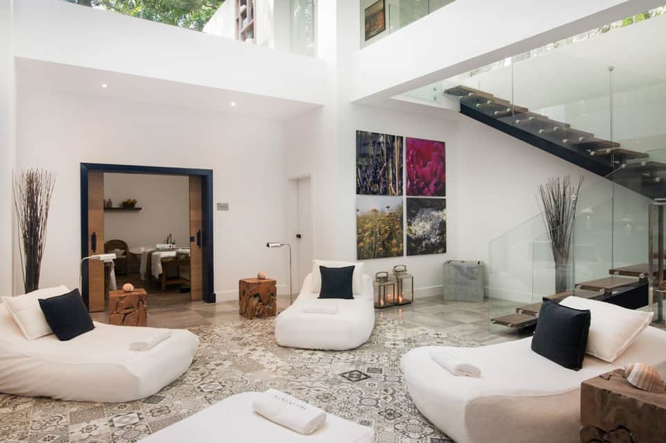 Luxury spa relaxation room with white curved seating, skylights, glass railings, and natural light
