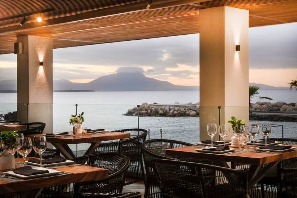 Fine dining restaurant with wooden tables, modern chairs, and mountain view over water at dusk