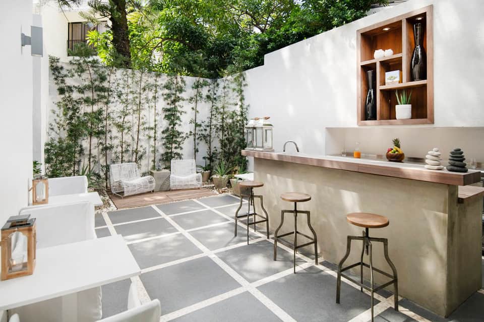 Contemporary outdoor patio with white walls, built-in bar, climbing vines, modern seating, and water feature