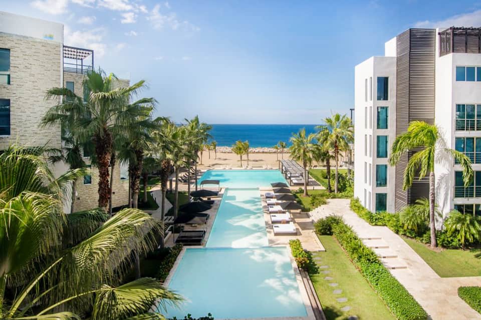 Resort courtyard with turquoise pool, palm trees, and modern white multi-story buildings